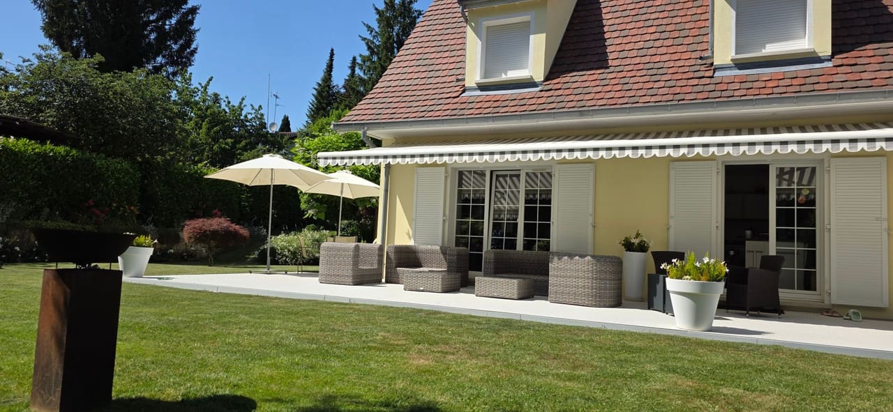 Maison près de Bâle à vendre : terrasse côté jardin avec store, parasols et salon de jardin face à la pelouse